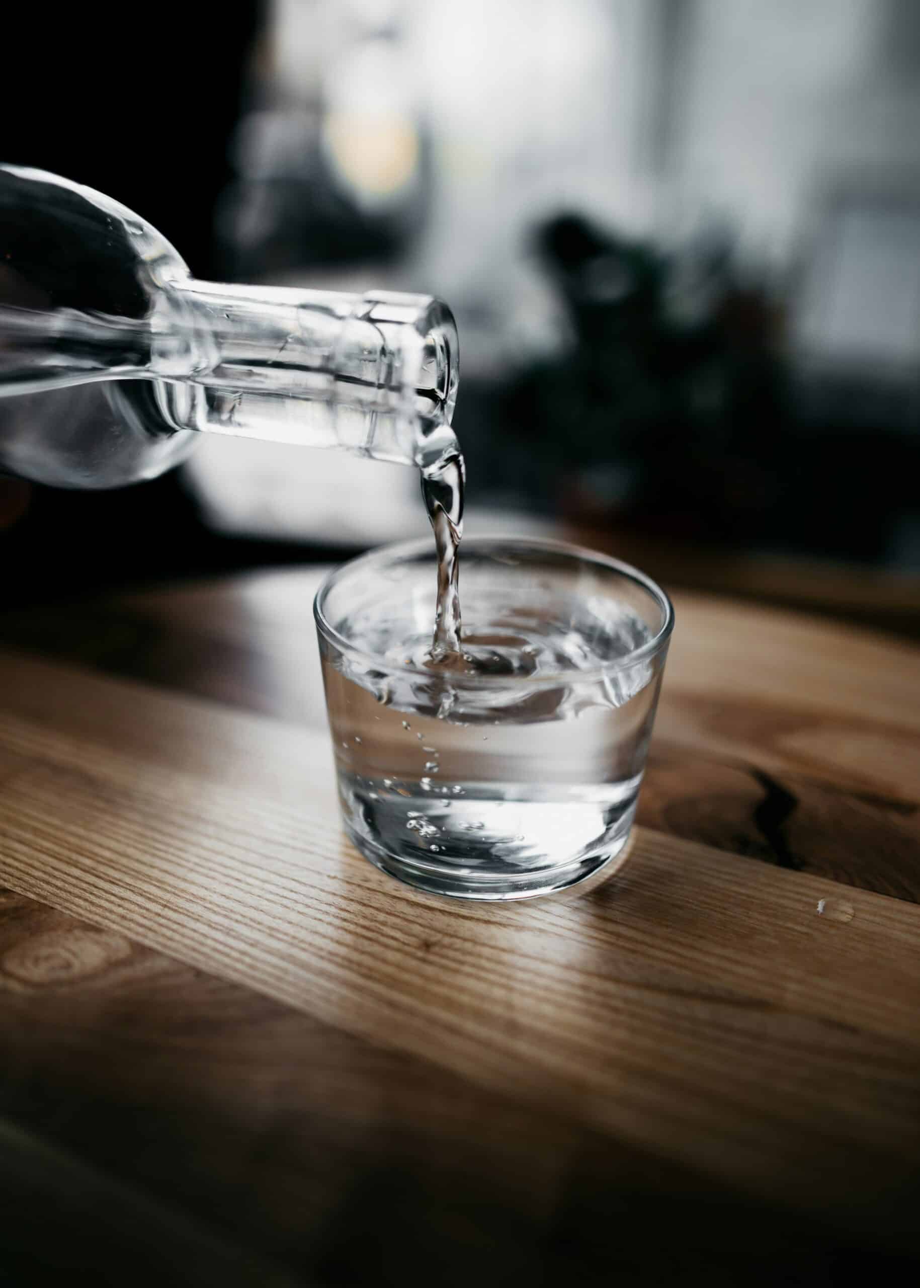 someone pouring purified drinking water from a bottle into a glass